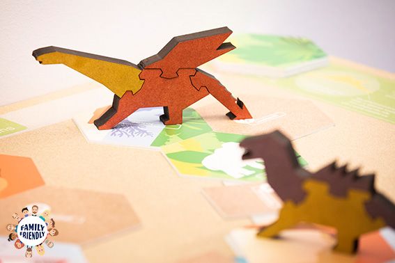 zwei orangefarbige Dinosaurier als Spielfiguren aus Holz auf einem Spielbrett