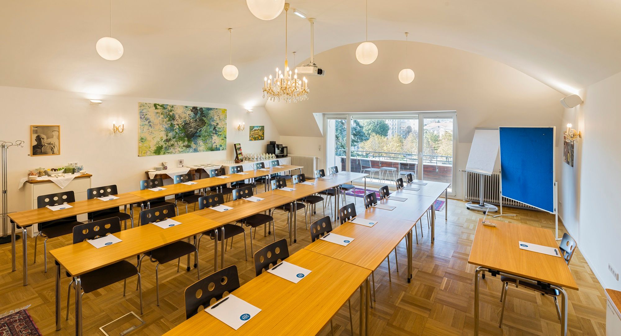 Ein Konferenzraum mit Tischen und Stühlen, einem Kronleuchter und einem großen Fenster mit Blick nach draußen.