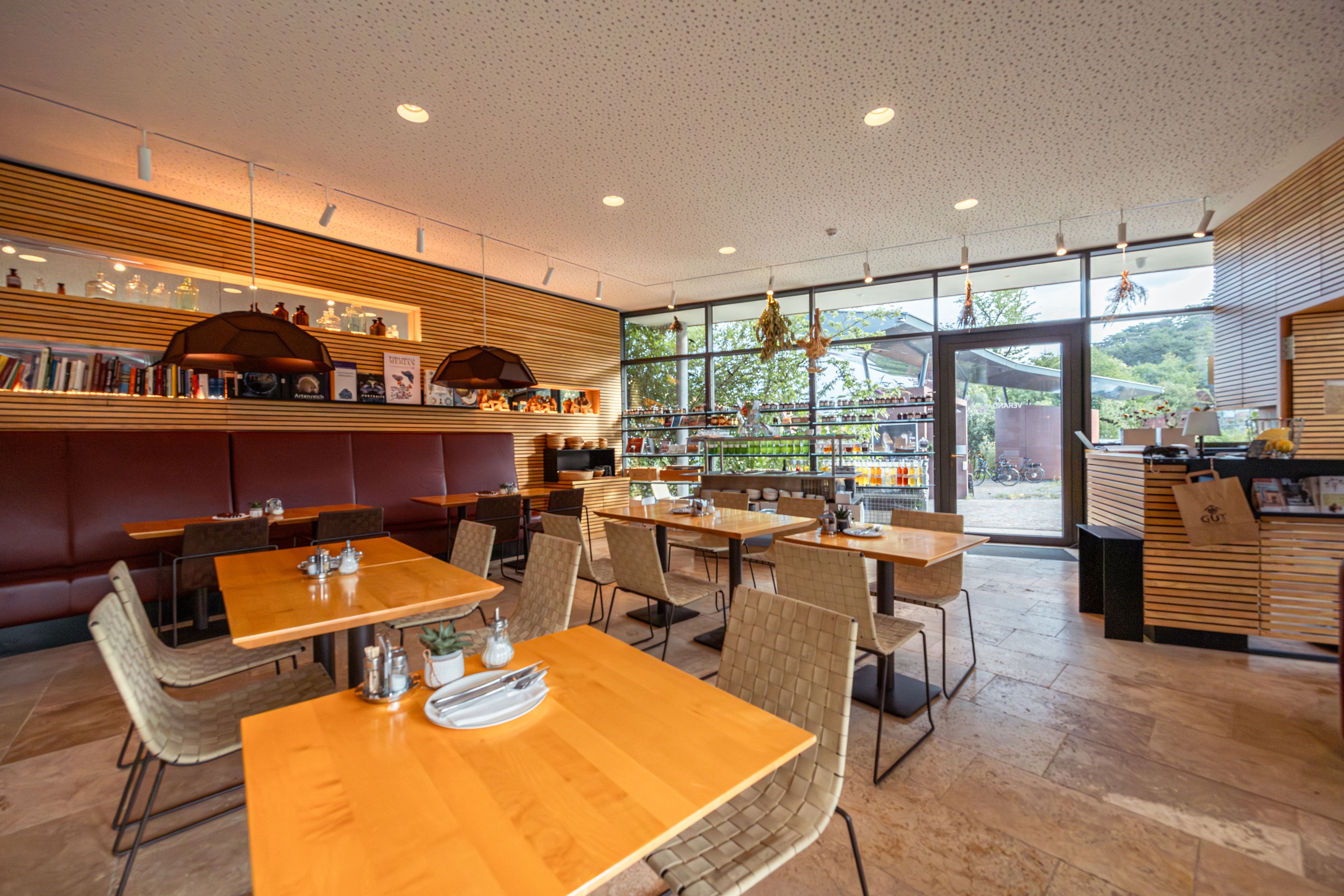 Innenansicht eines modernen Restaurants mit Holztischen und großen Fenstern.