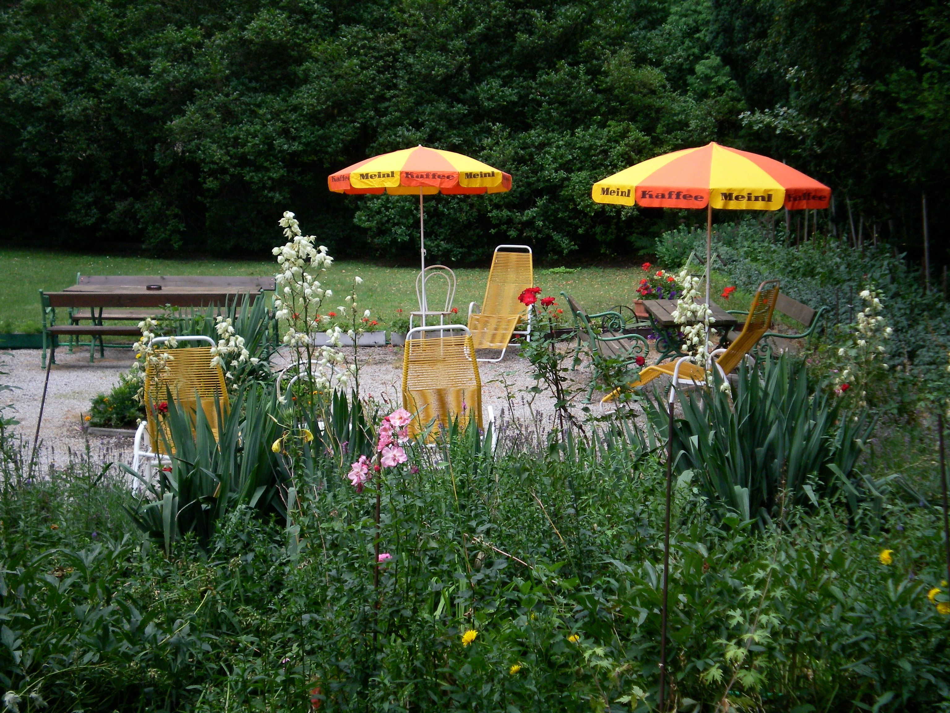 Garten mit gelben Liegestühlen und Sonnenschirmen, umgeben von Blumen und Bäumen.