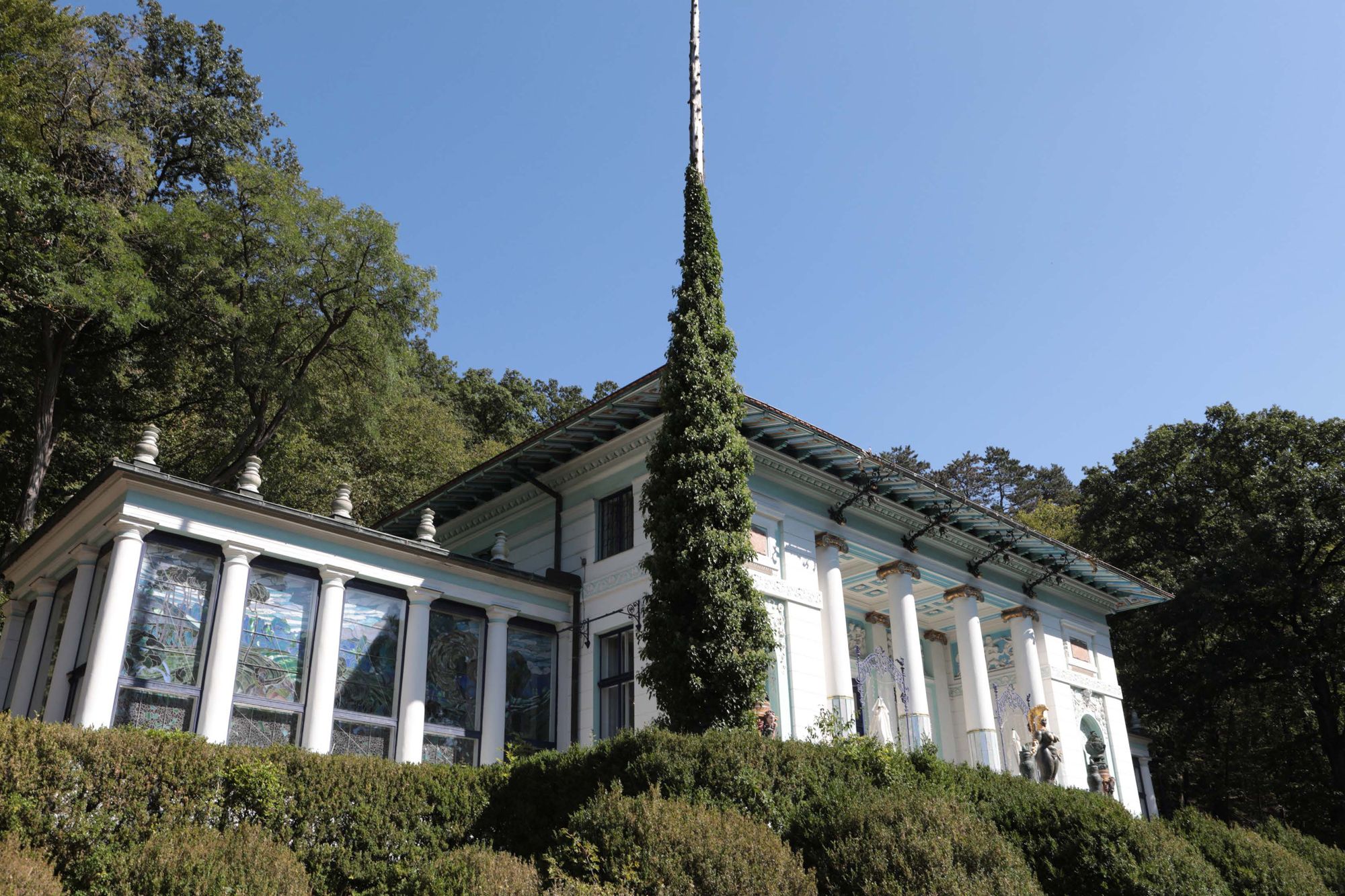 Ernst-Fuchs-Museum mit Säulen und Glasfenstern, umgeben von Bäumen.
