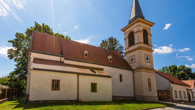 Kirche mit Turm und rotem Dach in Winzendorf bei Sonnenschein.