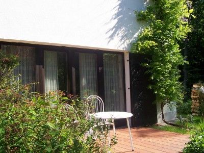 Terrasse mit Tisch und Stuhl vor einem Haus mit großen Fenstern.