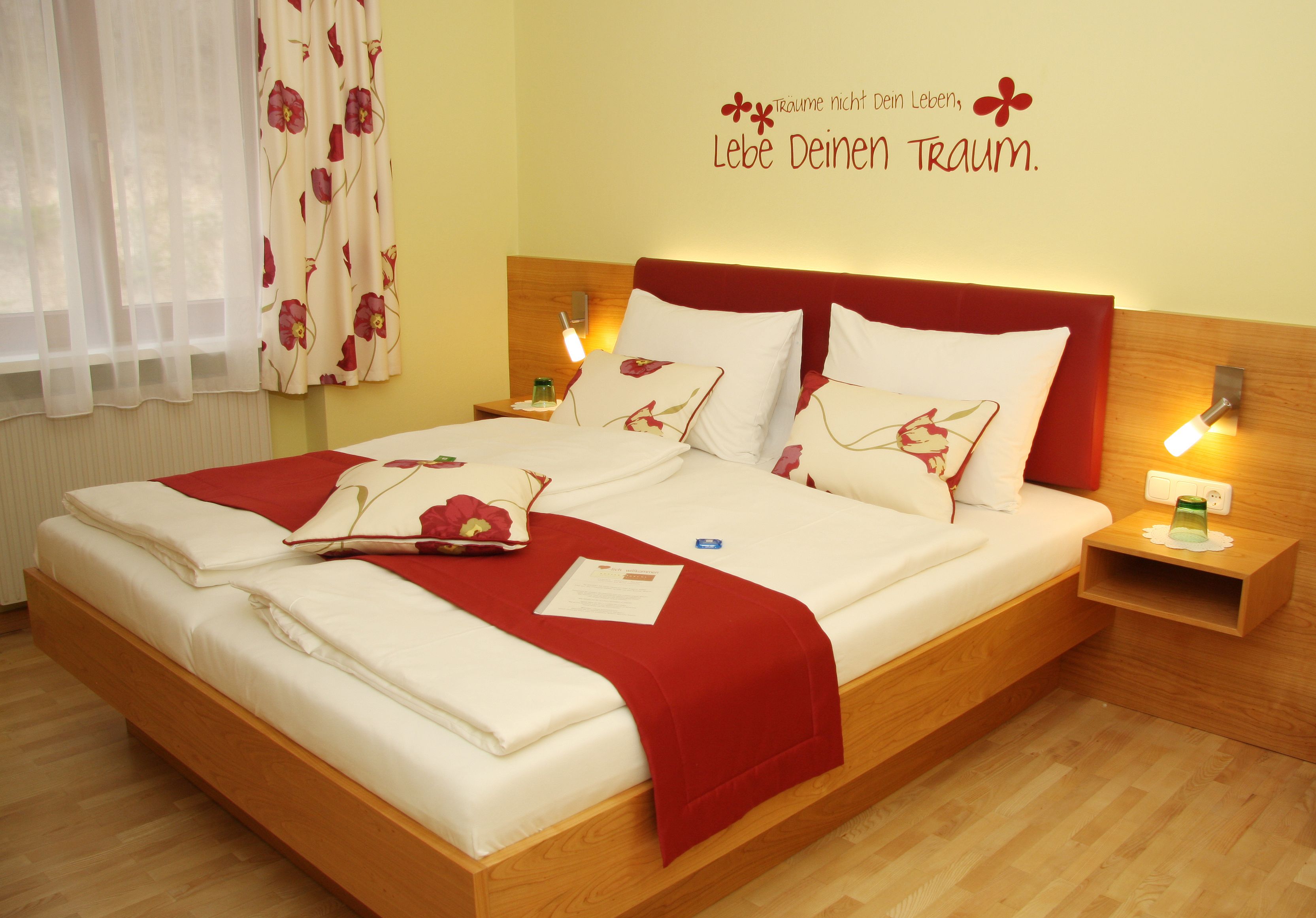 Ein gemütliches Hotelzimmer mit einem Doppelbett, roten Akzenten und einem inspirierenden Wandzitat.