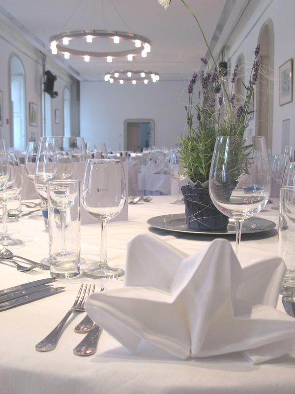 Eleganter Tisch mit weißer Tischdecke, Gläsern, Besteck und Lavendel-Dekoration in einem festlichen Raum.