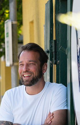 Gelbe Strahlkraft und ein Lächeln. Johannes Ley, lässig lehnend vor dem einladend gelb gefärbten Allerley, verkörpert die Freundlichkeit seines Restaurants. Ein starker Auftritt, der Aufmerksamkeit erweckt.