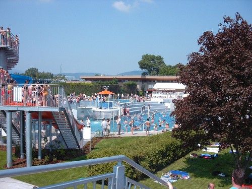 Ein belebtes Freibad mit vielen Menschen, Wasserrutschen und Liegewiese.