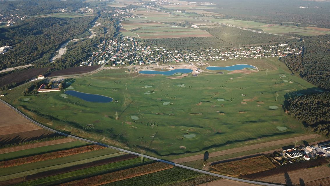 Luftaufnahme eines Golfplatzes mit mehreren Wasserhindernissen und angrenzender Siedlung.