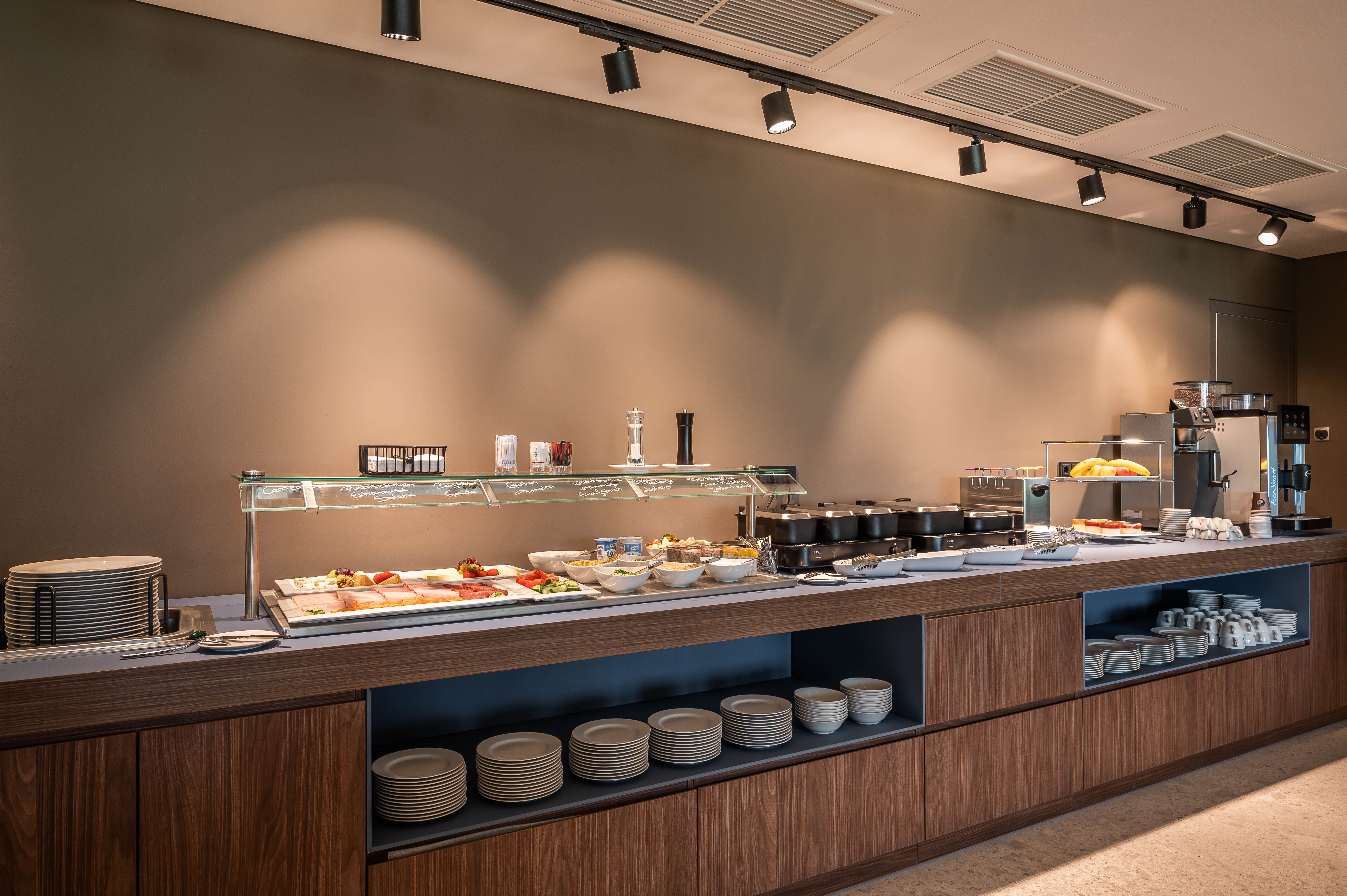 Ein Frühstücksbuffet mit verschiedenen Speisen und Geschirr in einem modernen Raum.