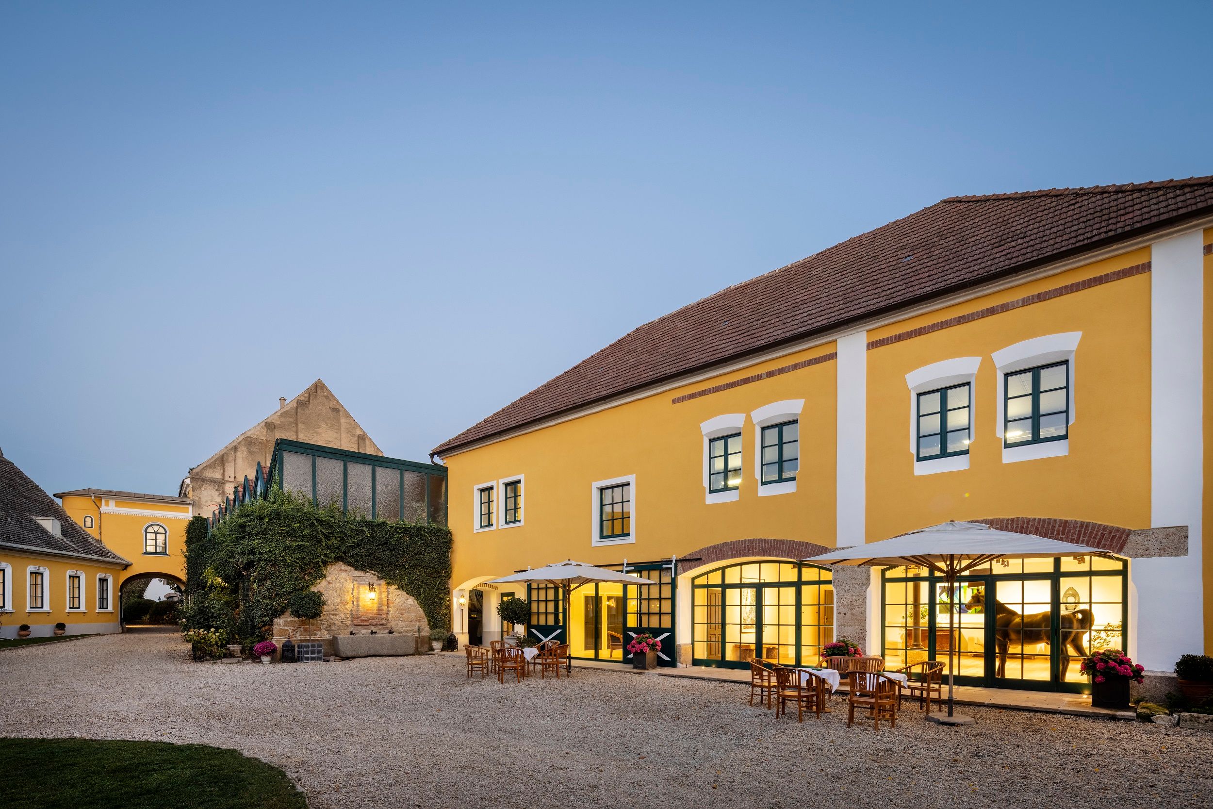 Yellow building with inner courtyard and outdoor tables at dusk.