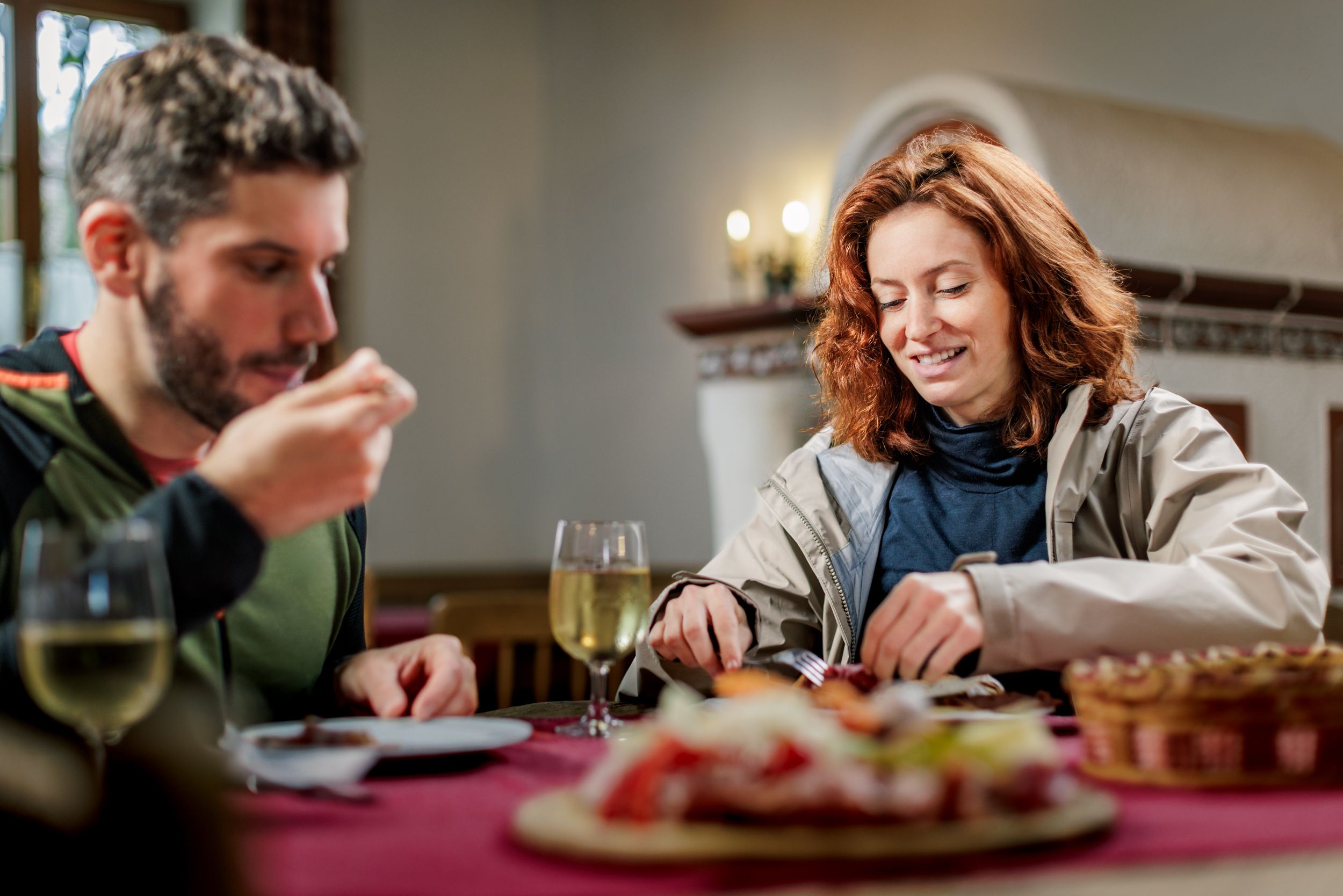 Ein Mann und eine Frau sitzen in einer Stube auf einem rustikalen Holztisch und essen eine Brettljause