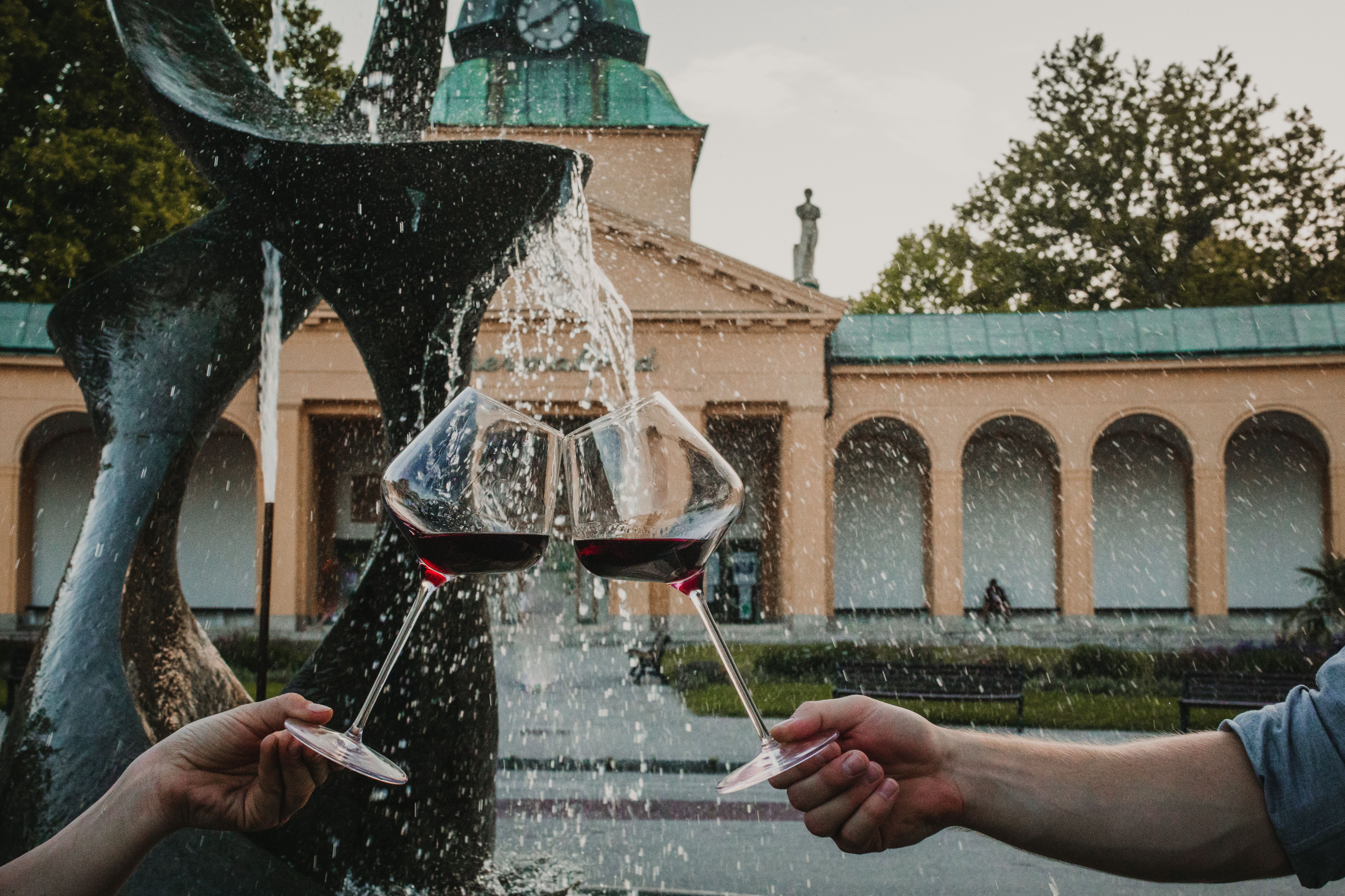 Zwei Gläser mit tiefrotem Wein werden fröhlich angestoßen, während das Wasser des Brunnens sanft plätschert. Umgeben von einer malerischen Landschaft, lädt dieser Ort dazu ein, die kulinarischen Köstlichkeiten der Region zu genießen und die Seele baumeln zu lassen.
