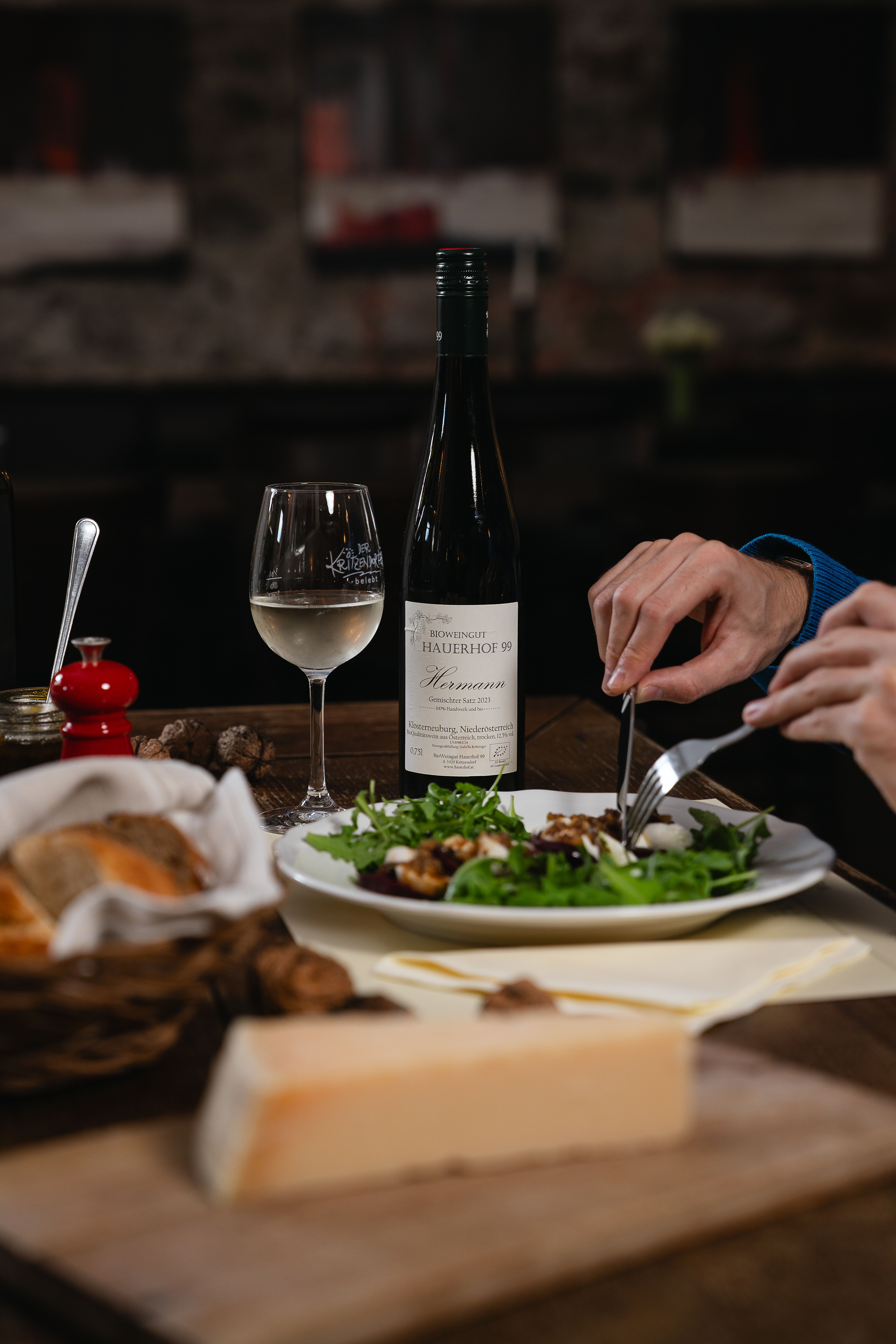 Eine Flasche Gemischter Satz neben einem Glas Wein, begleitet von einem liebevoll angerichteten Rucola-Salat mit Mozzarella, Parmesankäse und Brot.