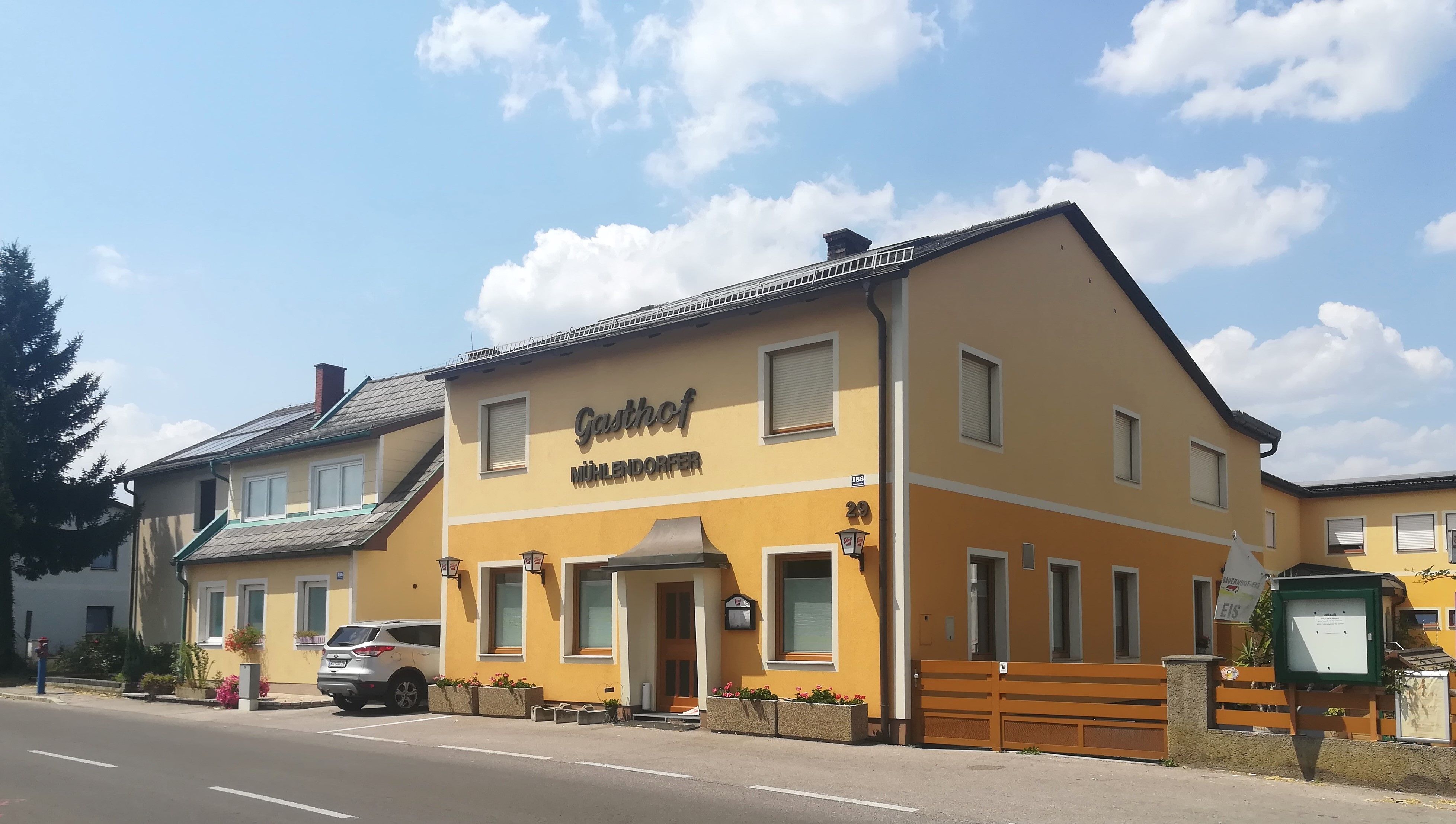 Ein gelbes Gebäude mit der Aufschrift 'Gasthof Mühlendorfer' an einer Straße.