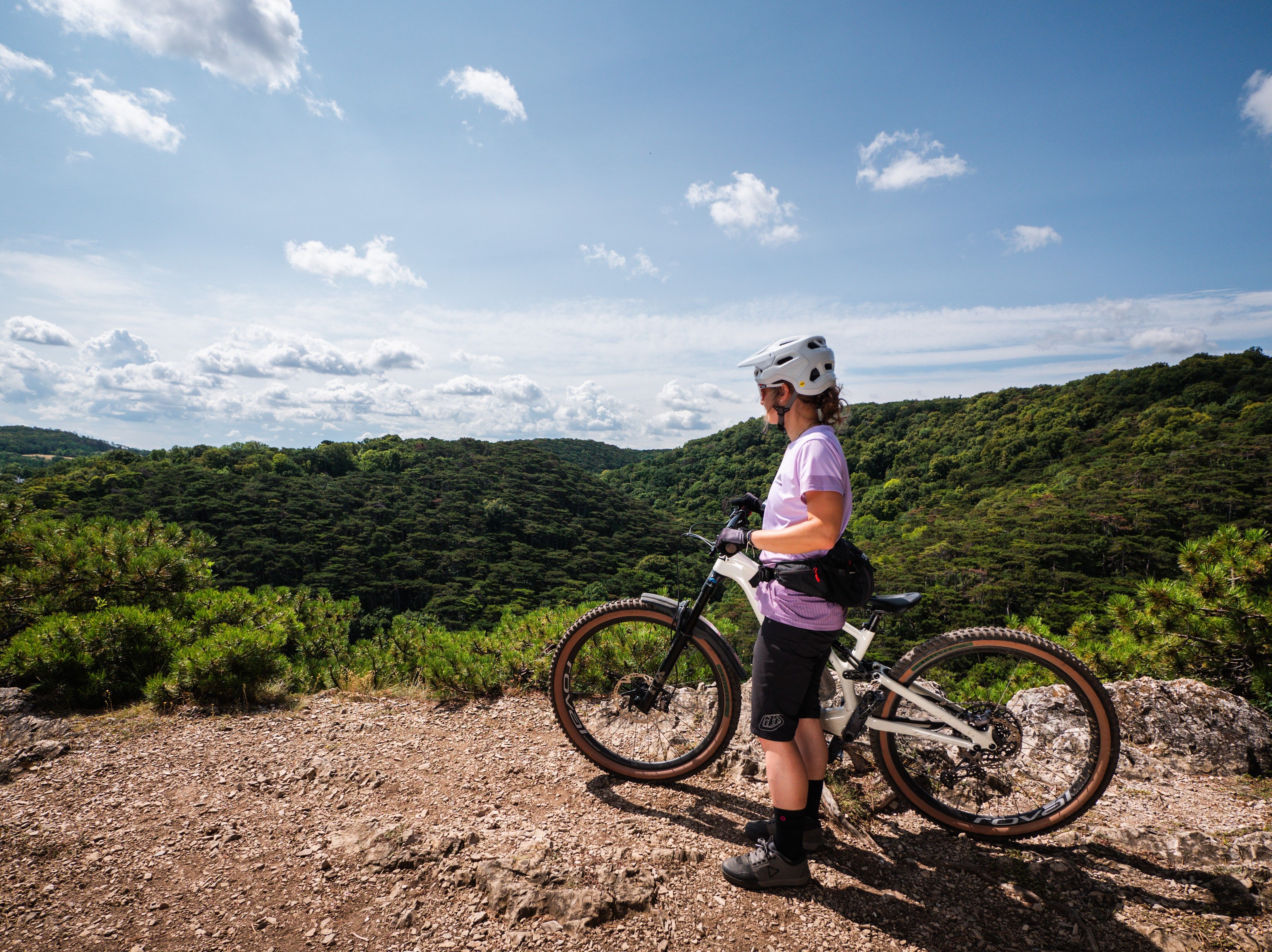 Ein Mountainbiker genießt die atemberaubende Aussicht auf die sanften Hügel und dichten Wälder des Wienerwaldes. Die frische Luft und die Ruhe der Natur laden zu einem unvergesslichen Abenteuer ein. Hier, wo die Freiheit der Berge spürbar wird, ist jeder Moment ein Genuss.