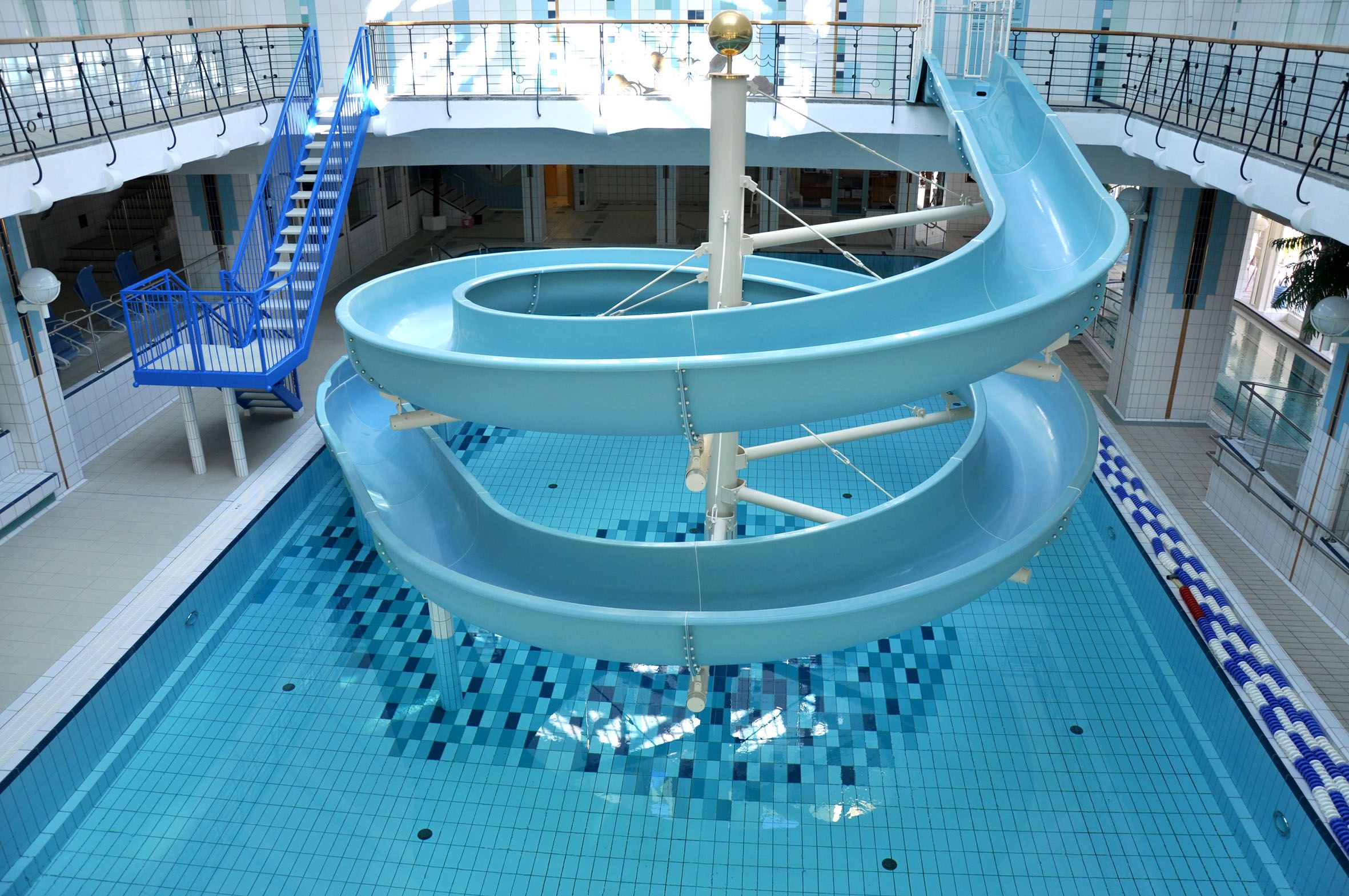 Innenansicht eines Hallenbads mit blauer Wasserrutsche und Schwimmbecken.