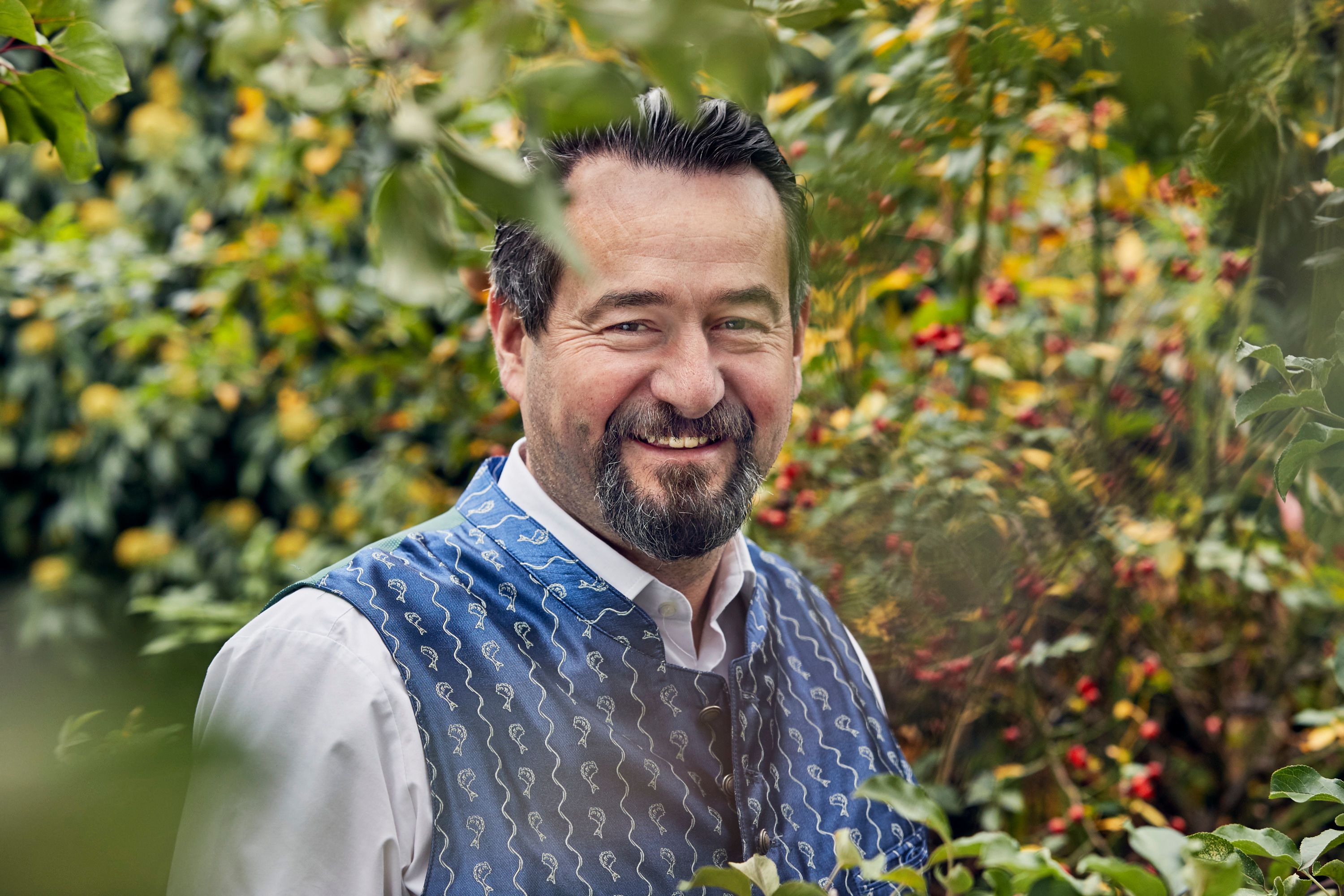 Ein Mann in traditioneller Kleidung lächelt in einem Garten.