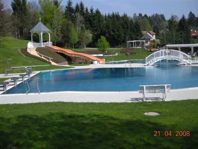 Freibad mit Rutsche, Brücke und Pavillon im Hintergrund.