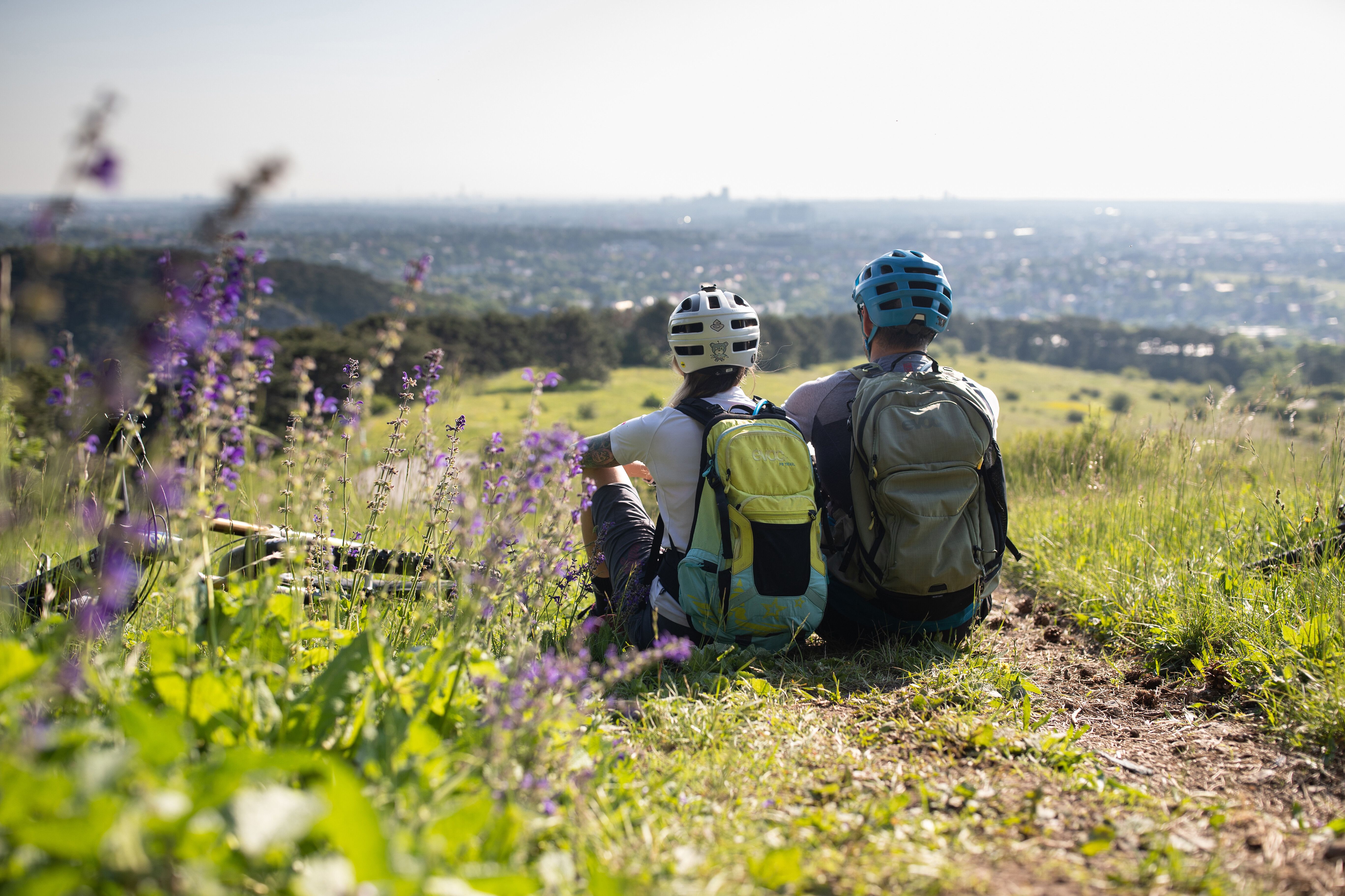In der warmen Sommerluft genießen zwei Mountainbiker die atemberaubende Aussicht auf die sanften Hügel und das weite Tal. Umgeben von bunten Wildblumen und dem sanften Rauschen des Windes, ist dies der perfekte Ort, um eine wohlverdiente Pause einzulegen und die Schönheit der Natur zu erleben.