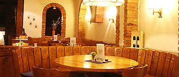 Gemütliches Stüberl mit Holztisch und Stühlen, umgeben von rustikalen Backsteinbögen und warmem Licht.