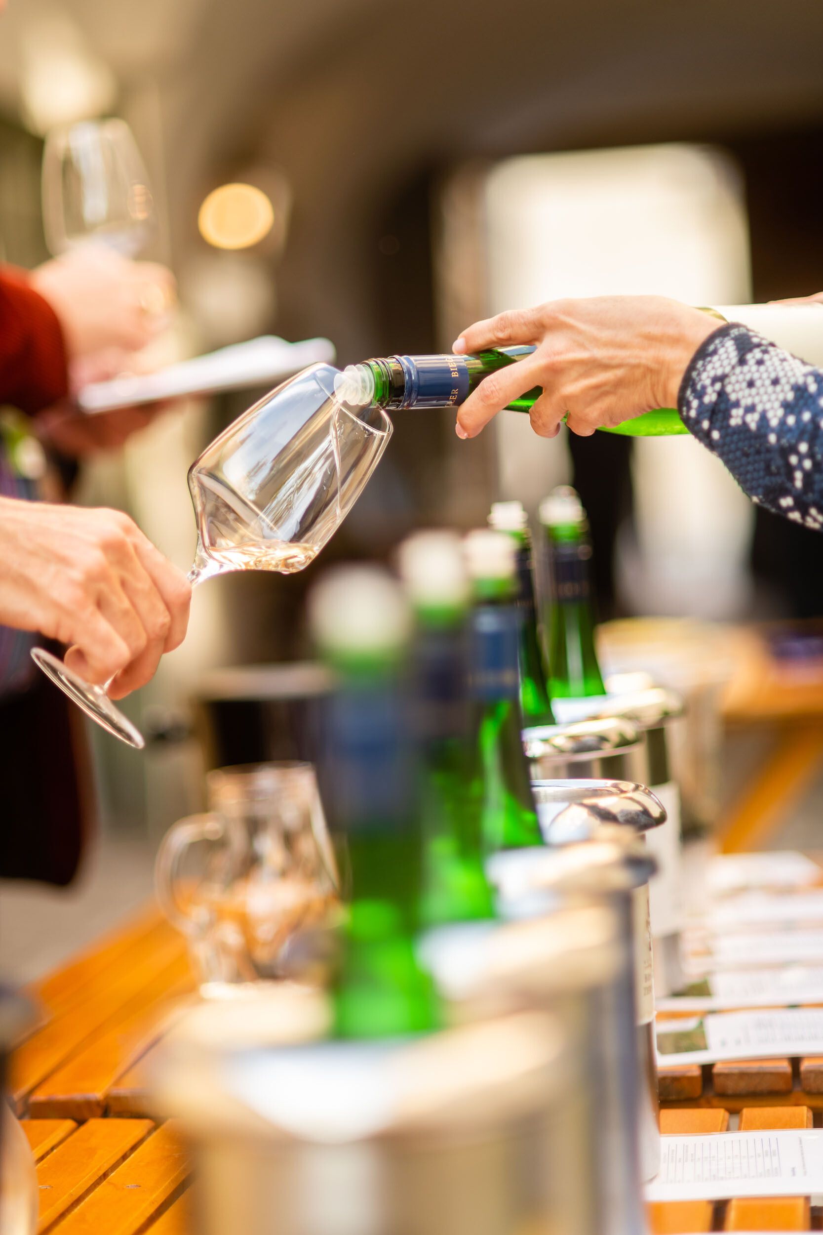 Inmitten der malerischen Weinlandschaft wird ein Glas erlesener Wein eingeschenkt, während die Gäste in geselliger Runde anstoßen. Die sanften Hügel des Wienerwaldes umrahmen die Szenerie und laden dazu ein, die Aromen des Weins und die Schönheit der Natur zu genießen.