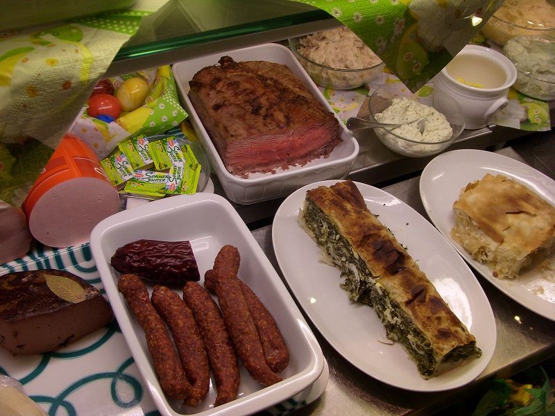 Verschiedene Speisen auf einem Buffet, darunter Fleisch, Würste und Strudel.