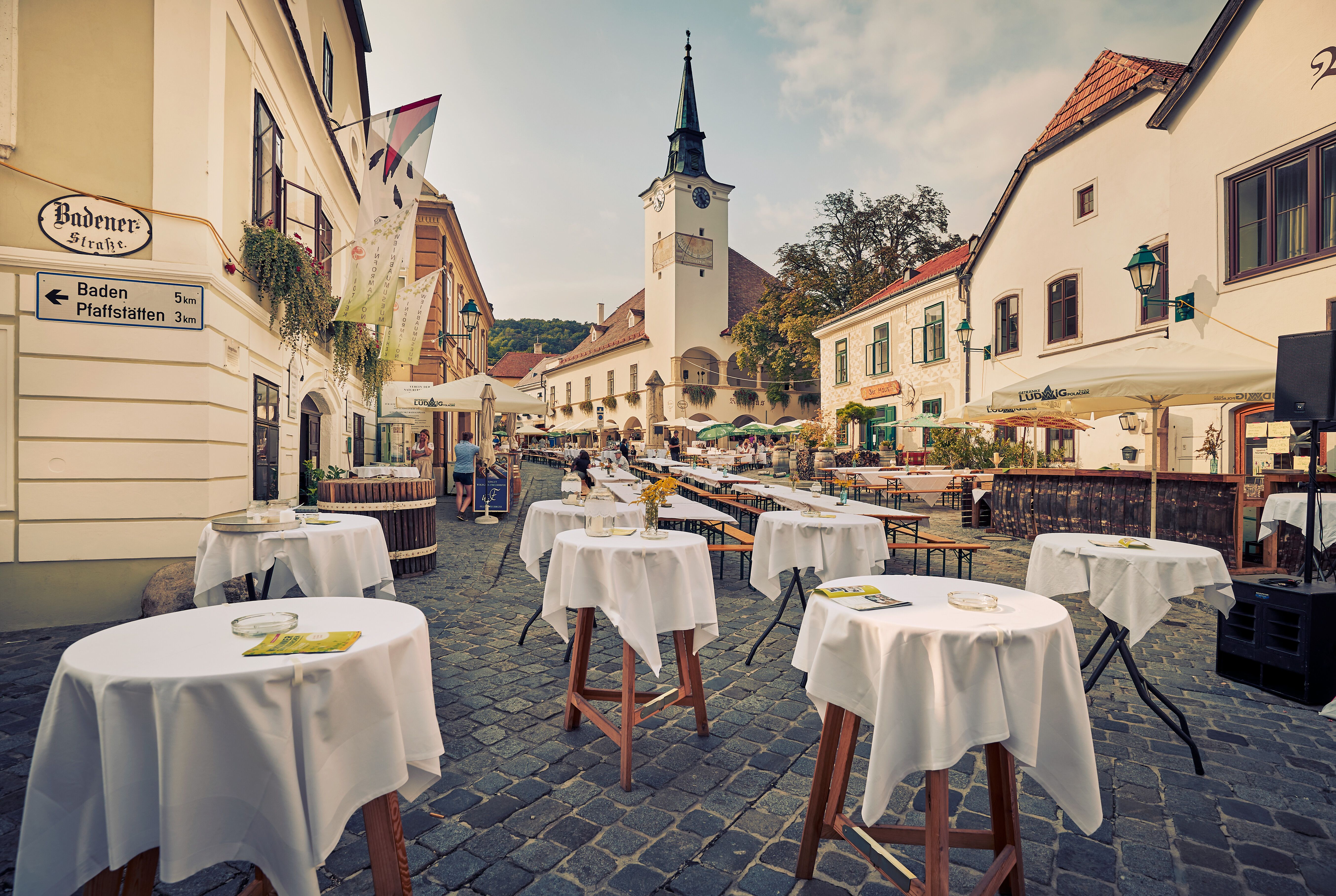 Die malerische Straße lädt ein, die Seele baumeln zu lassen, während die Tische auf fröhliche Gäste warten. Umgeben von sanften Hügeln und Weinreben, verspricht dieser Ort unvergessliche Momente voller Genuss und Geselligkeit.