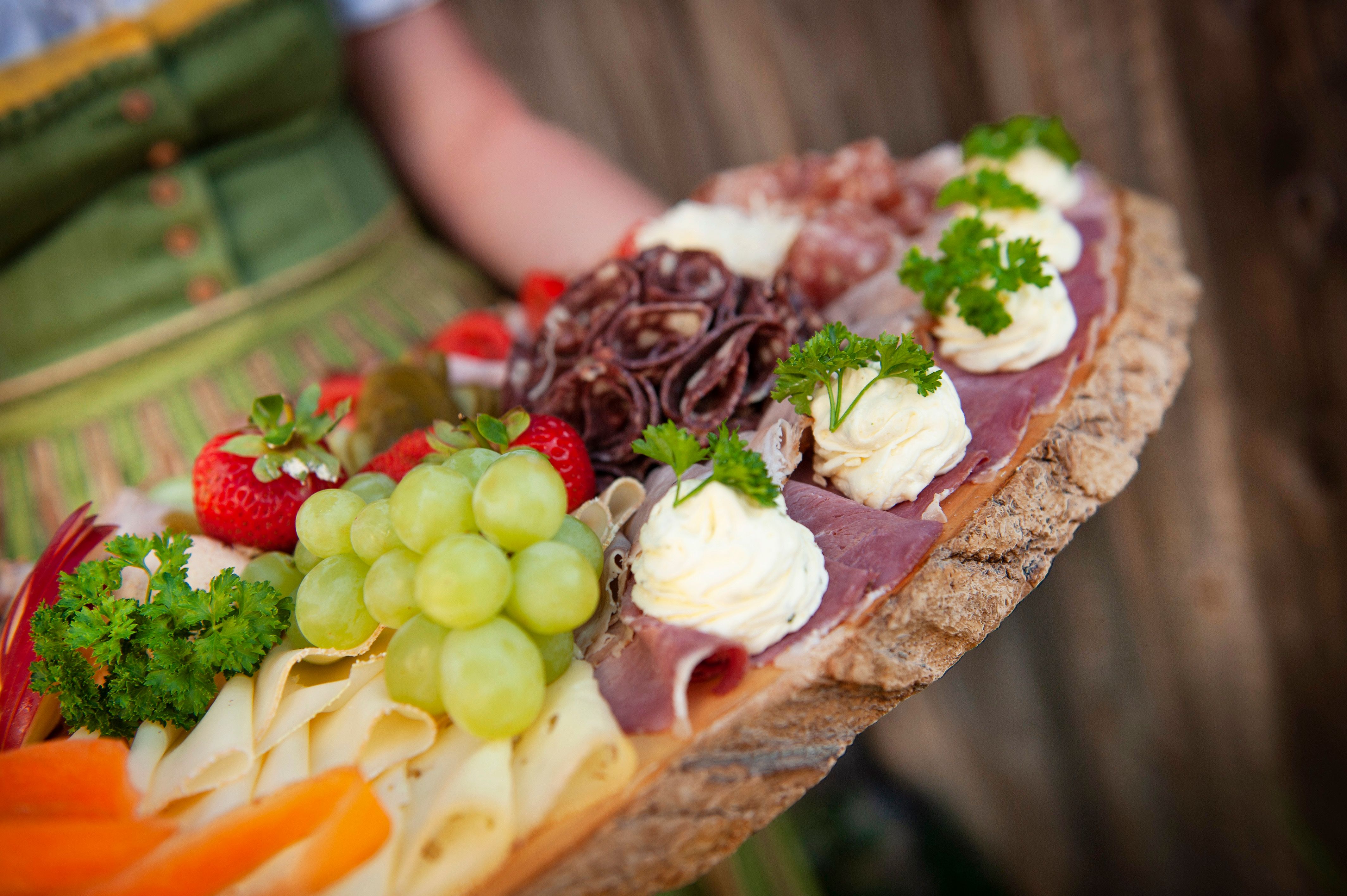 Eine rustikale Platte mit Käse, Schinken, Trauben, Erdbeeren und Kräutern.