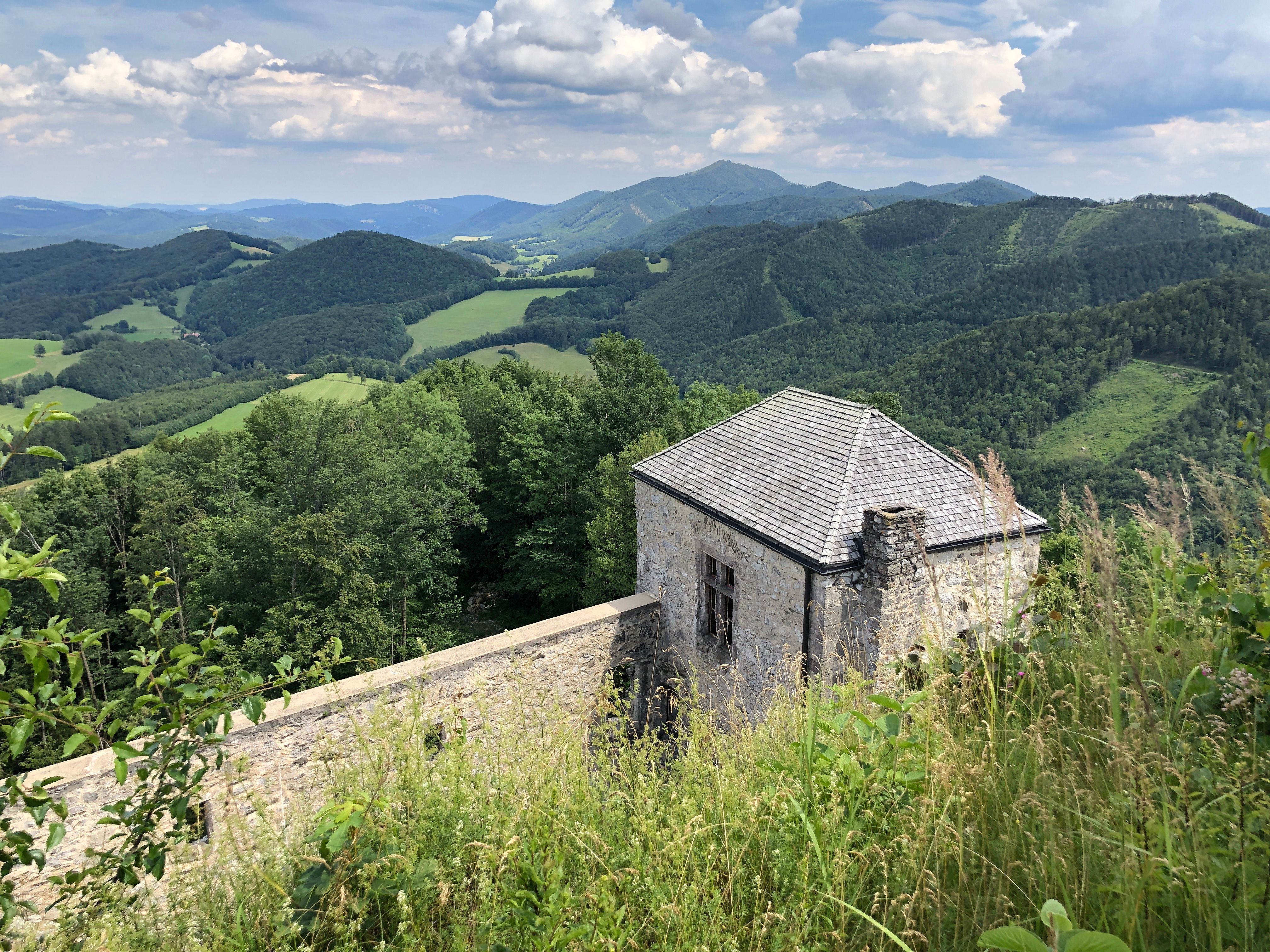 Mystisch erhebt sich die Ruine der Kaumberg auf einem felsigen Grund, umgeben von den stillen Hügeln des Triestingtals. Unter dem bewölkten Himmel erzählen die alten Mauern und der tapfere Wehrturm von längst vergangenen Zeiten. Vor der Burg ziehen sich steinige Pfade durch die blühenden Wiesen, ein Versprechen von Abenteuer und Entdeckung. 