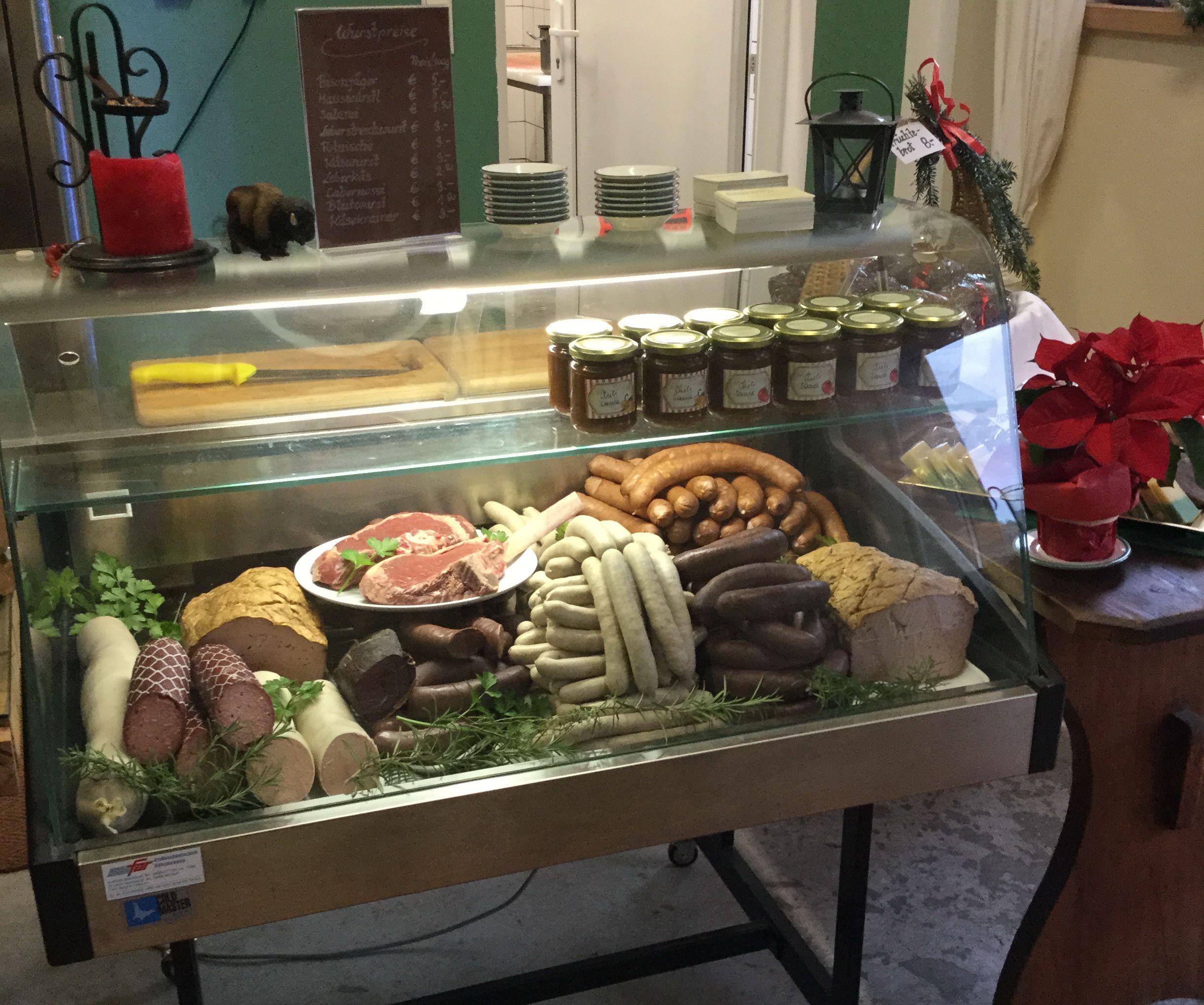 Eine Fleischtheke in einem Hofladen mit verschiedenen Wurstsorten, Fleischstücken und Gläsern mit Aufstrichen.