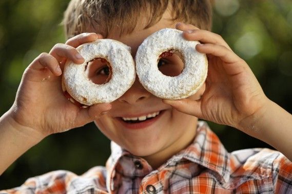 Ein Junge hält zwei mit Puderzucker bestreute Donuts vor seine Augen.