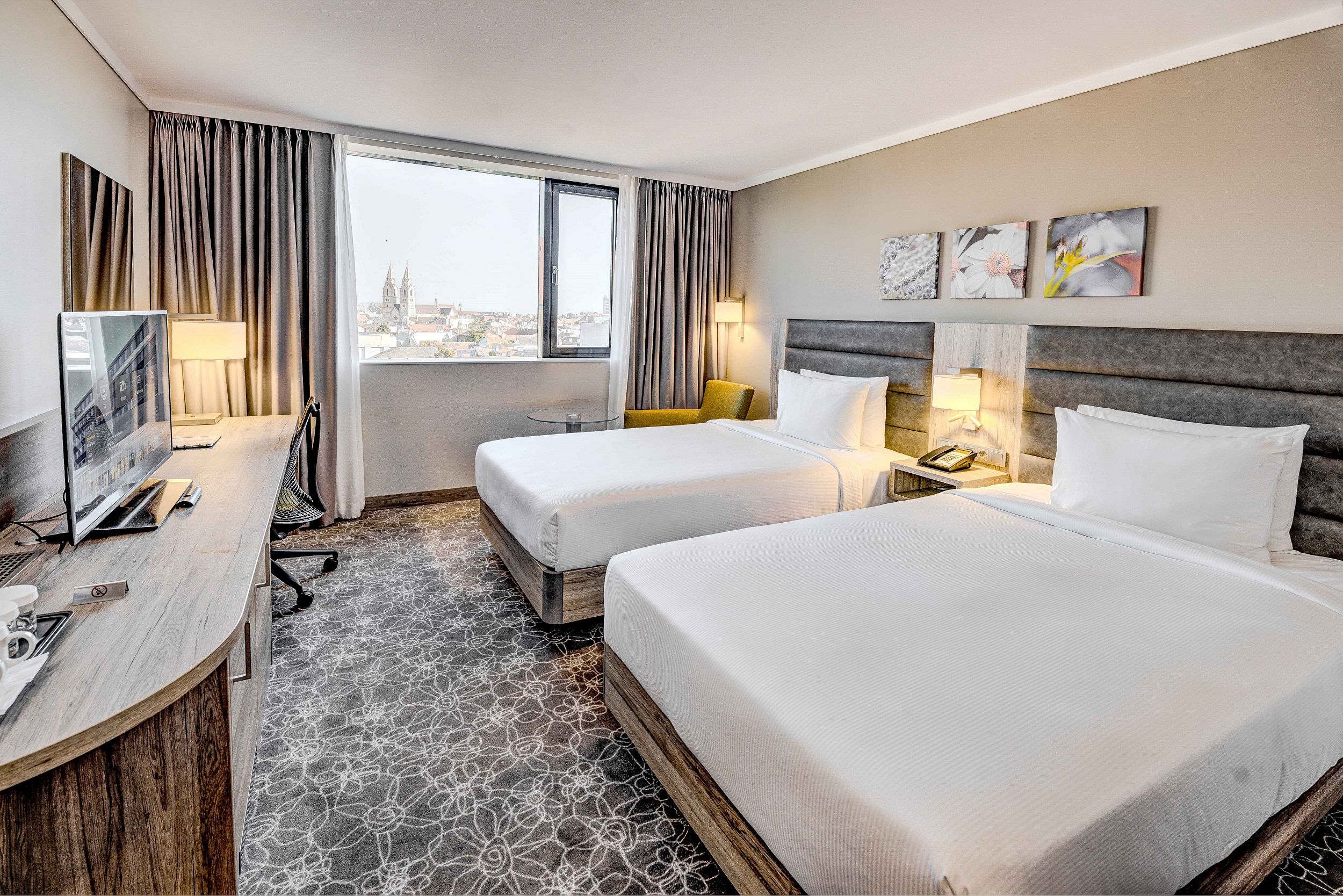 Hotelzimmer mit zwei Betten, Schreibtisch und Fenster mit Stadtblick.