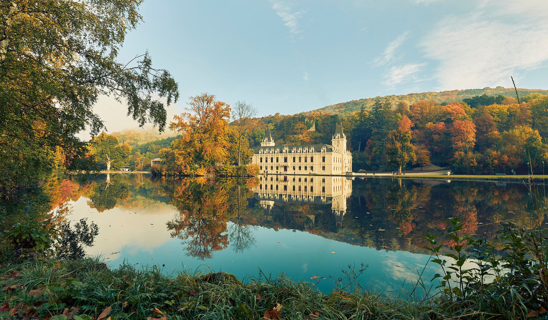 Umgeben von bunten Herbstblättern spiegelt sich das majestätische Schloss Hernstein im ruhigen Wasser des Sees wider. Die sanften Hügel im Hintergrund laden zu einem entspannenden Spaziergang ein, während die frische Luft die Sinne belebt.