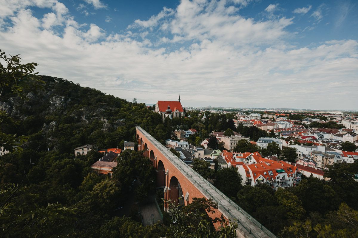Blick auf Mödling aus der Vogelperspektive und das Aquädukt sowie die Pfarrkirche St. Othmar an einem warmen Tag in der Dämmerung.