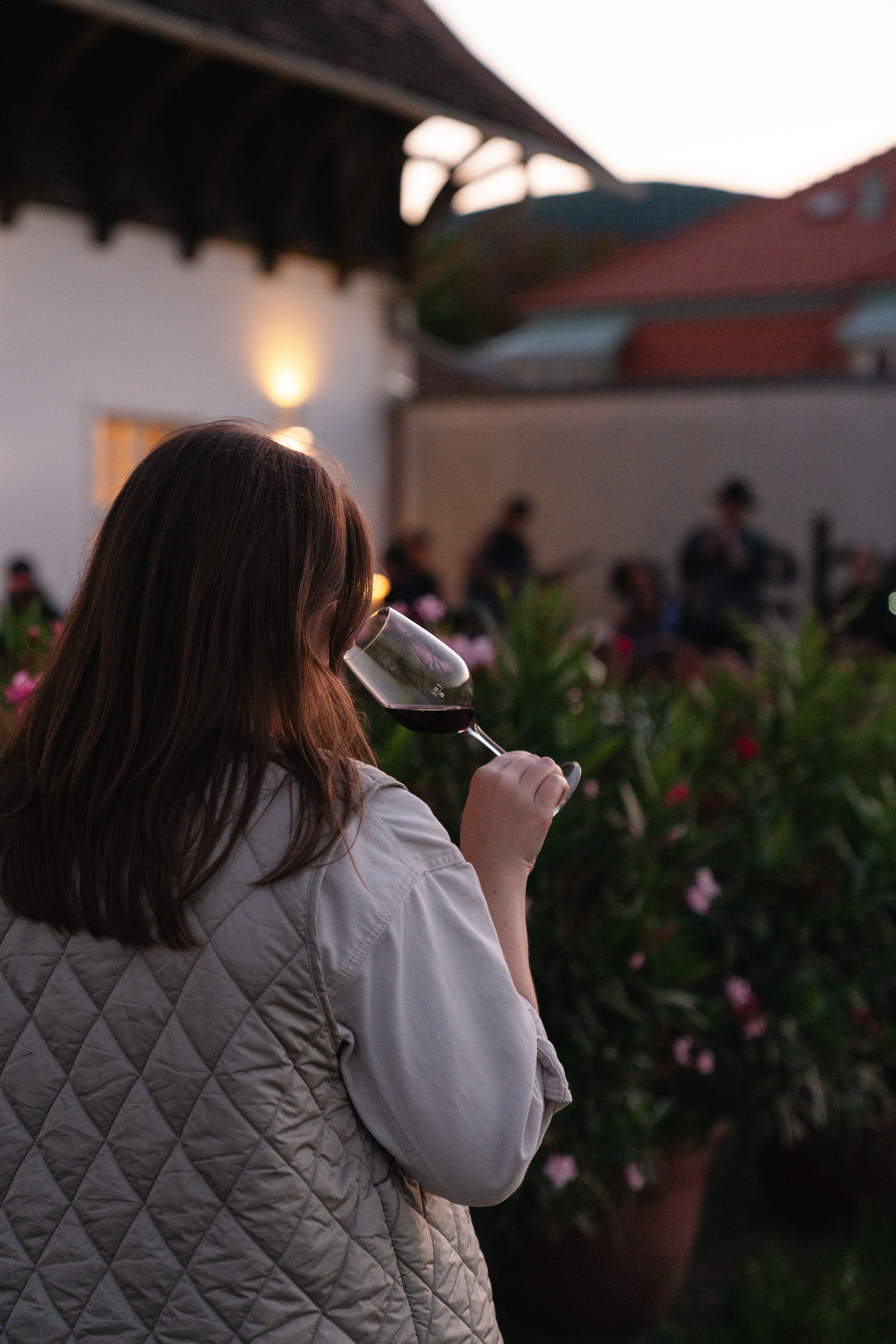 In der sanften Abenddämmerung genießt eine Person ein Glas Wein, während die blühenden Pflanzen um sie herum eine einladende Atmosphäre schaffen. Die harmonische Verbindung von Natur und Kulinarik lädt dazu ein, die regionalen Köstlichkeiten zu entdecken und die Seele baumeln zu lassen.