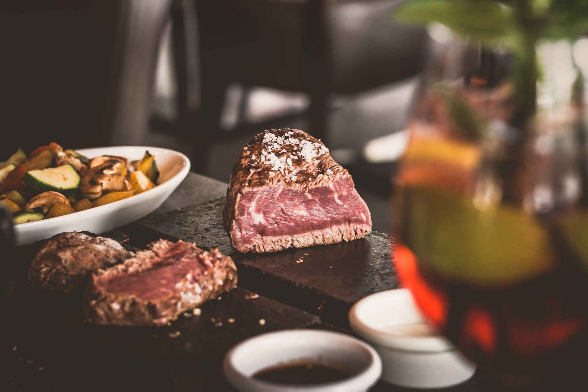 Ein saftiges Steak auf einem heißen Stein, begleitet von Gemüse und Soßen in Schälchen.