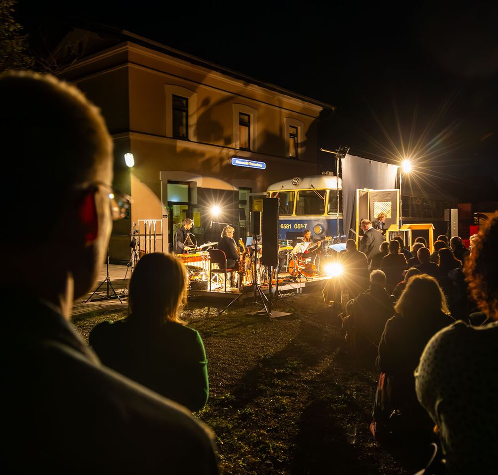 Unter dem funkelnden Sternenhimmel versammeln sich Menschen, um die Klänge eines einzigartigen Kulturabends zu genießen. Die warmen Lichter der Bühne schaffen eine einladende Atmosphäre, während die sanfte Brise die Vorfreude auf das bevorstehende Erlebnis verstärkt.