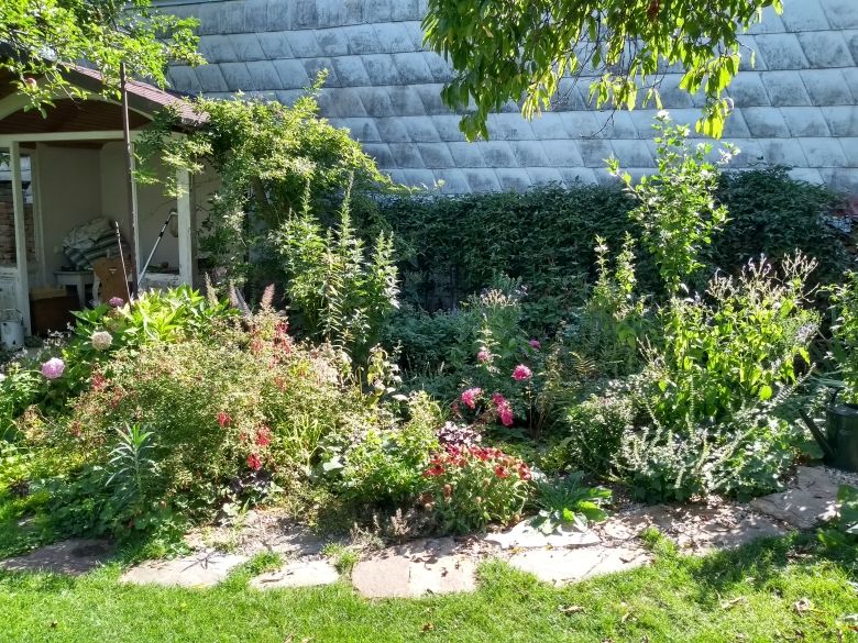 Ein blühendes Staudenbeet vor einer Mauer mit verschiedenen Pflanzen und Blumen.
