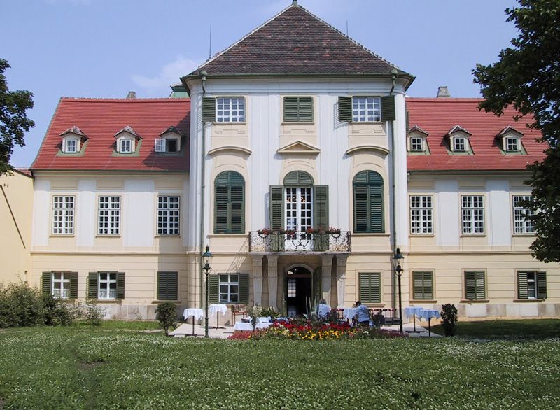 Frontansicht von Schloss Hunyadi mit Garten und Blumenbeeten.