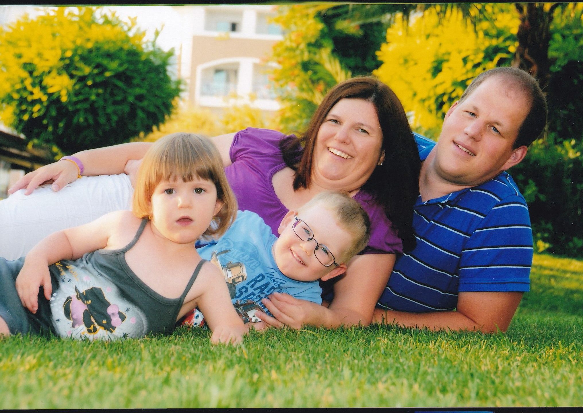 Eine Familie liegt lächelnd auf einer Wiese, bestehend aus zwei Erwachsenen und zwei Kindern.