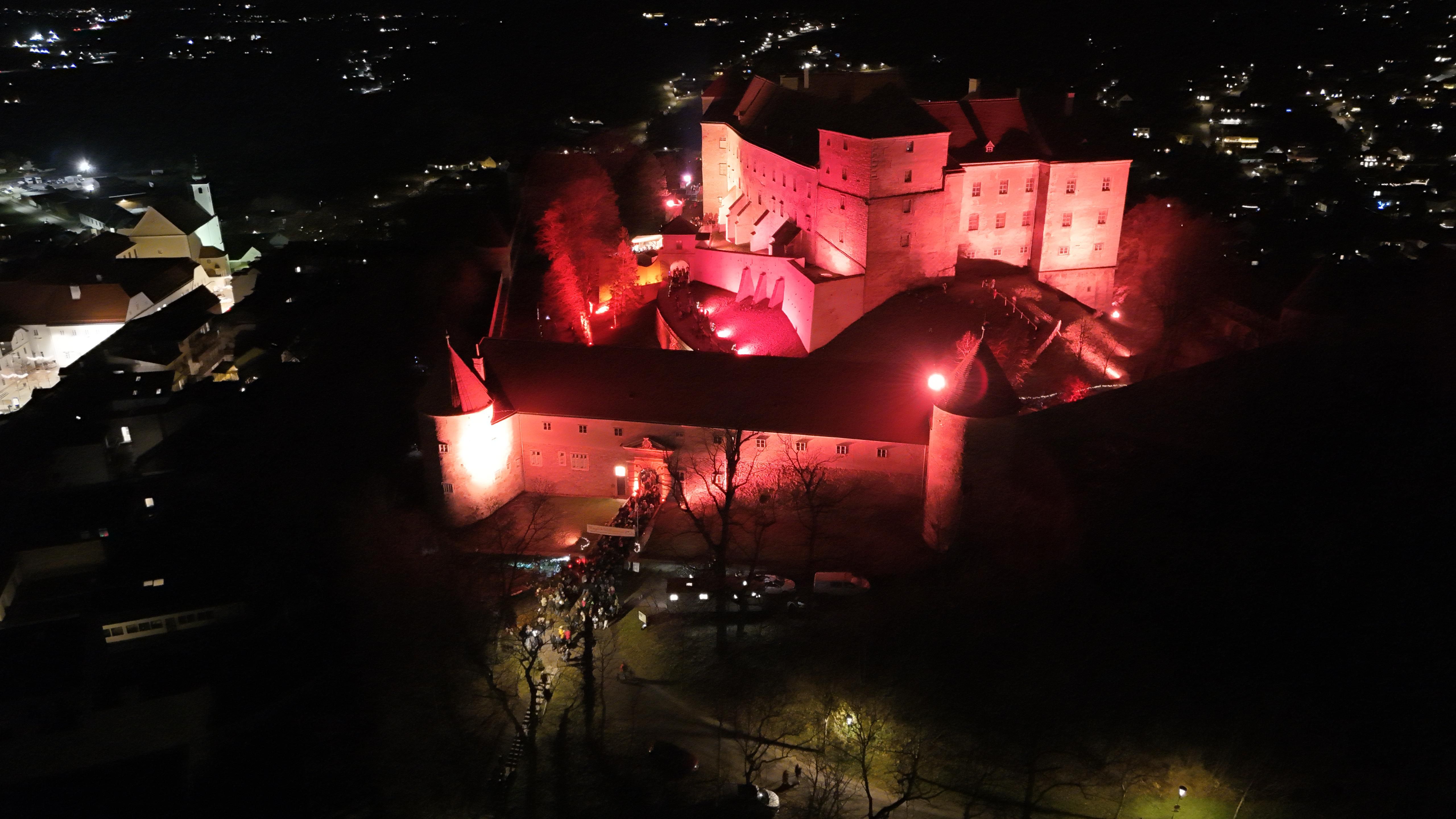 Vogelperspektive in der Dunkelheit, rötlich beleuchtetes Burgareal Neulengbach mit Blick auf den Weihnachtsmarkt.