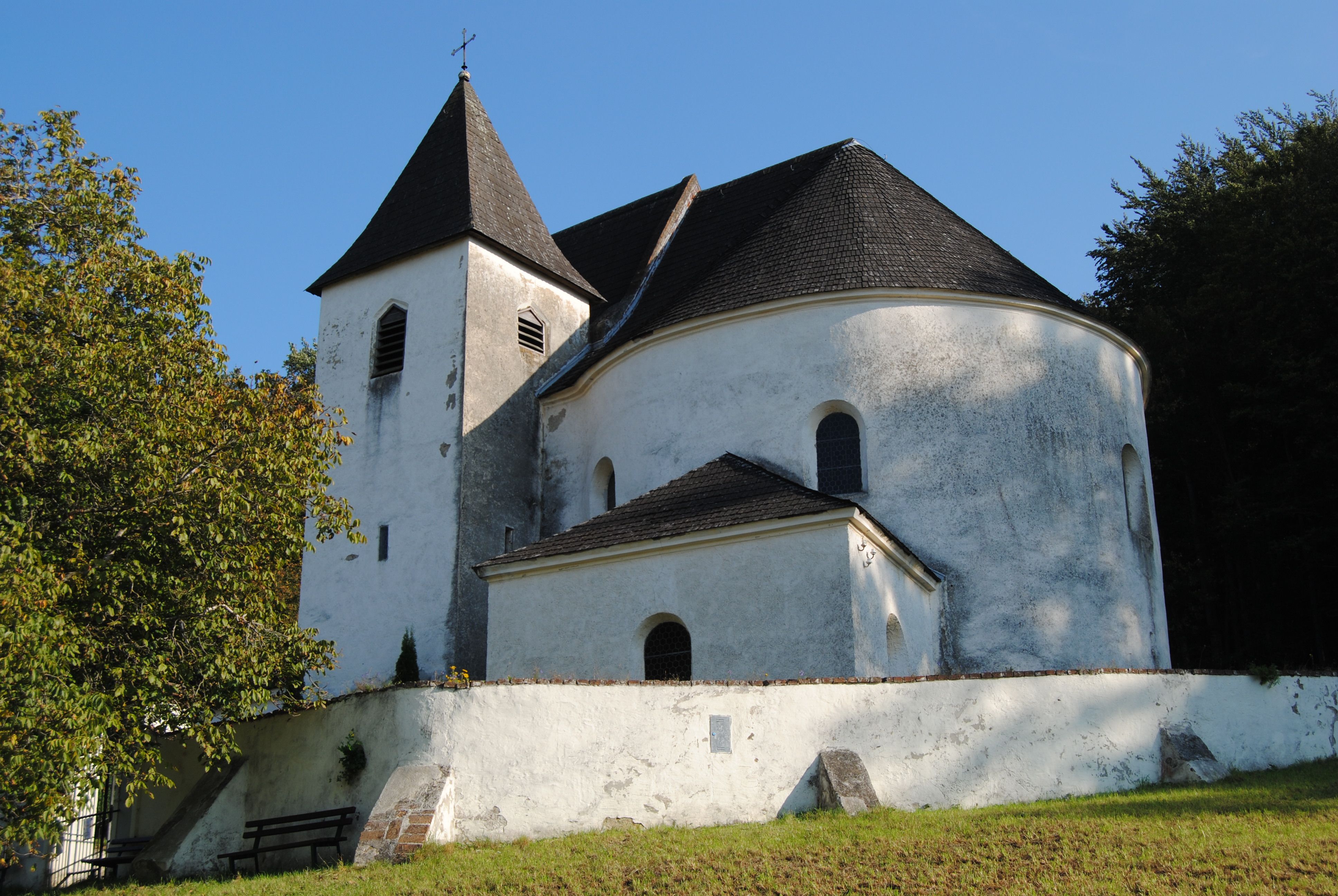 Weiße Kirche mit Turm und abgerundetem Dach, umgeben von Bäumen.