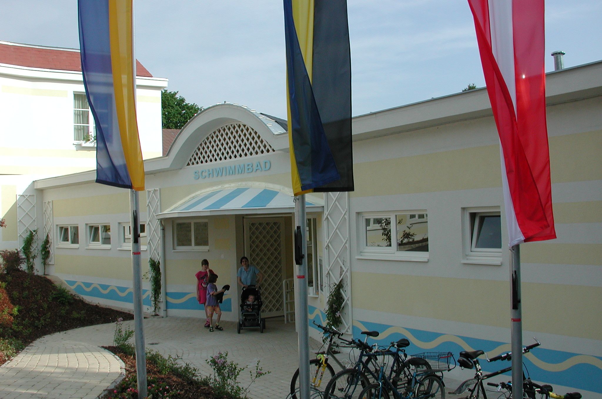 Eingang eines Schwimmbads mit Flaggen und Fahrrädern davor.