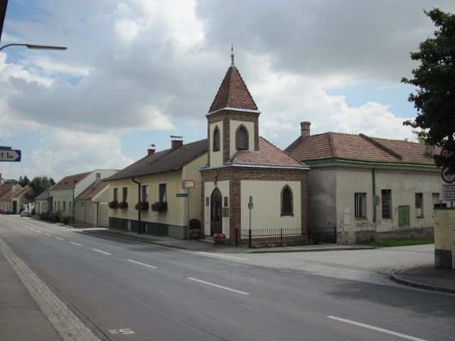 Straße in Lanzendorf mit Kirche und Wohnhäusern.