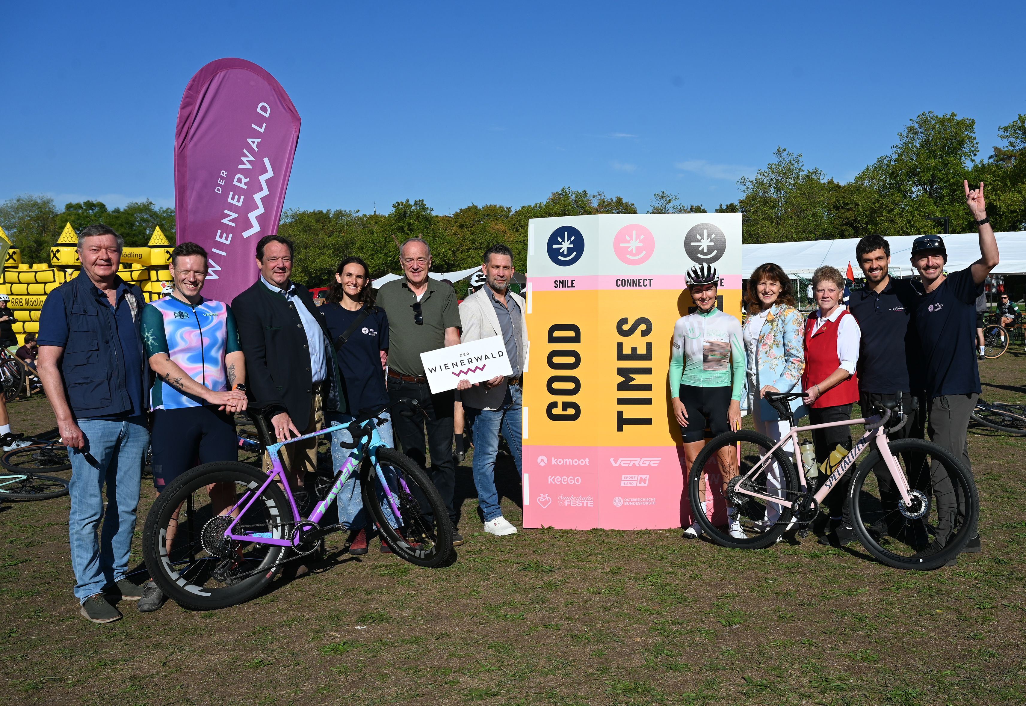 Gruppenfoto von Vertreterinnen und Vertretern der Veranstaltungsorganisation und der Region Wienerwald mit Gravelbikes und Veranstaltungsbannern im Hintergrund.