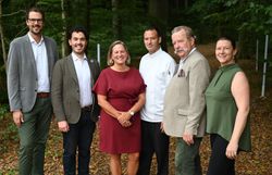 Gruppe von Personen steht vor einem Wald für ein Gruppenfoto