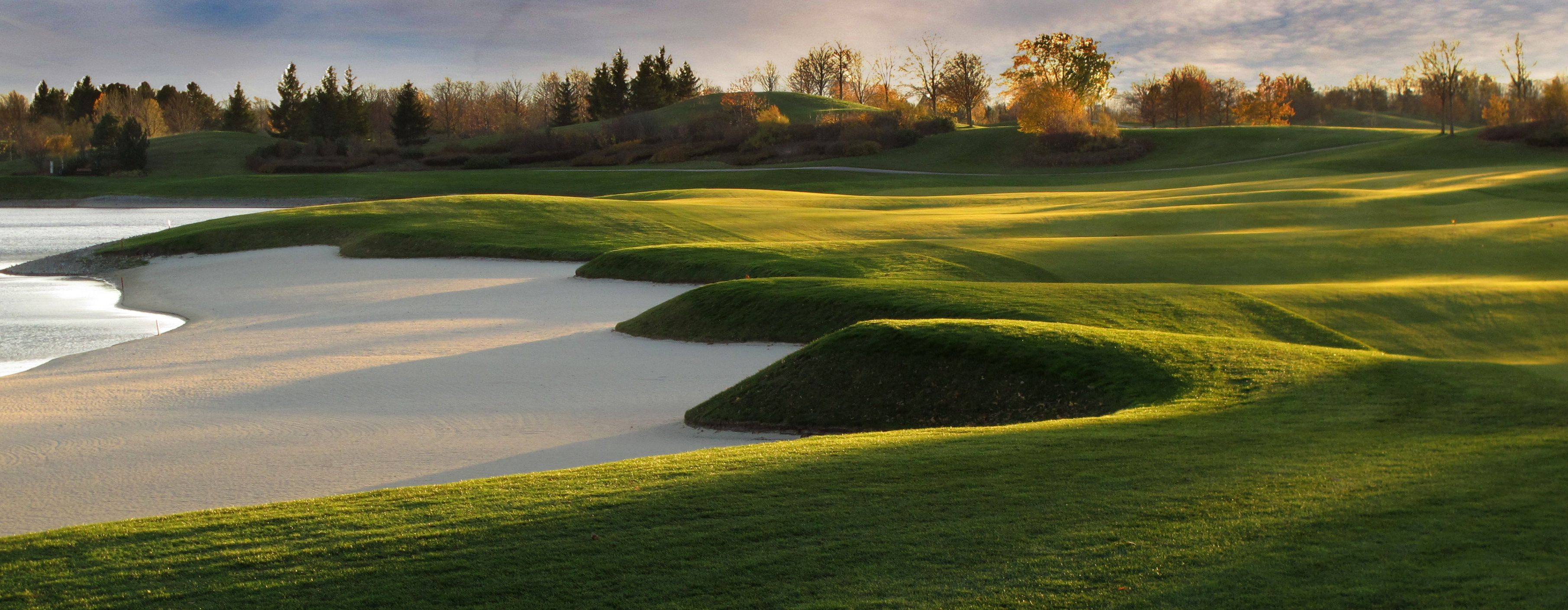 Panorama eines Golfplatzes mit Sandbunkern und grünen Hügeln im Sonnenlicht.