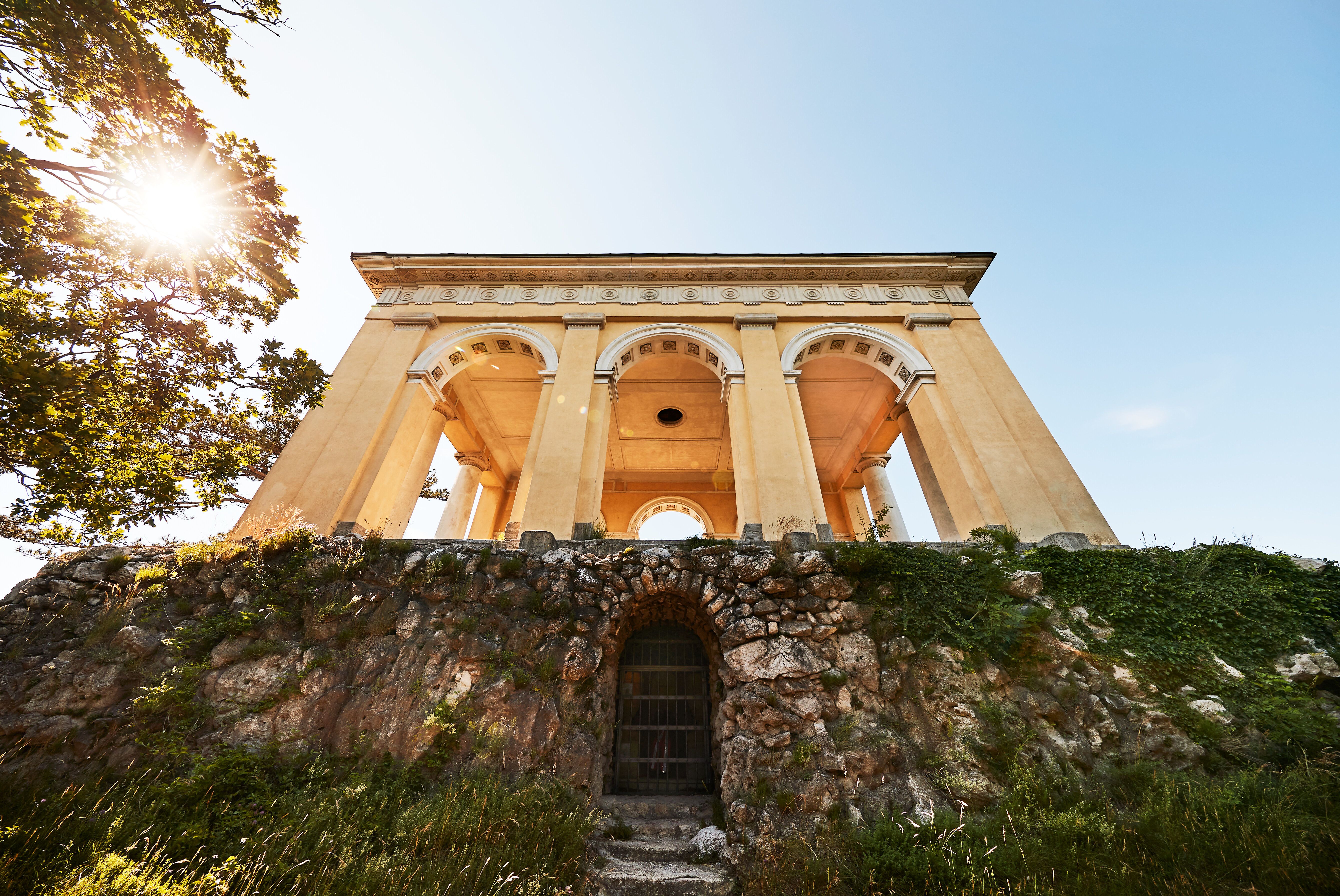 Der Husarentempel thront majestätisch über der Landschaft und bietet einen atemberaubenden Blick auf die umliegenden Wälder. Die warmen Sonnenstrahlen tauchen die historische Struktur in ein goldenes Licht, während die sanfte Brise die Blätter der Bäume zum Rascheln bringt. Ein Ort der Ruhe und Inspiration, ideal für einen unvergesslichen Ausblick.