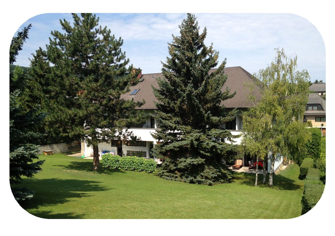 Rückansicht eines Gasthofs mit Garten und Bäumen.