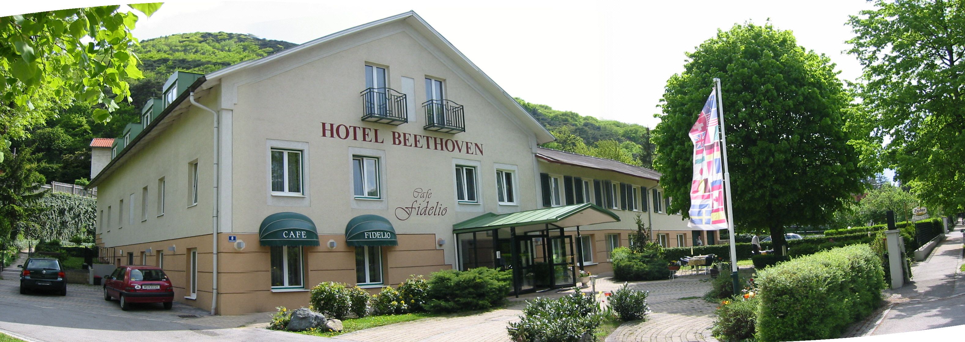 Außenansicht des Hotel Beethoven mit Café Fidelio, umgeben von Bäumen und Flaggen.